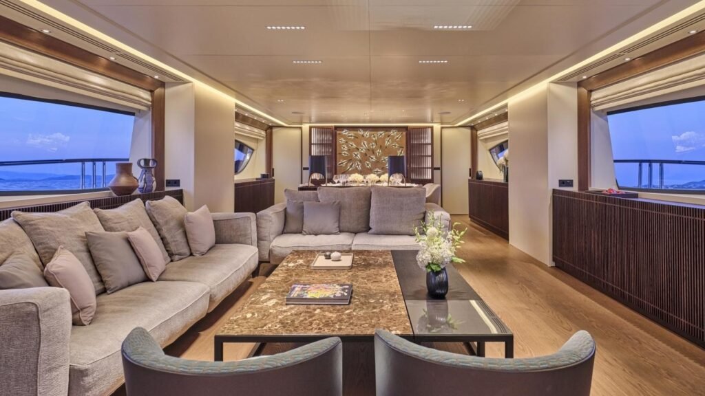 Main salon aboard ONCE MORE with twin sectionals and bronze-ringed oval windows
